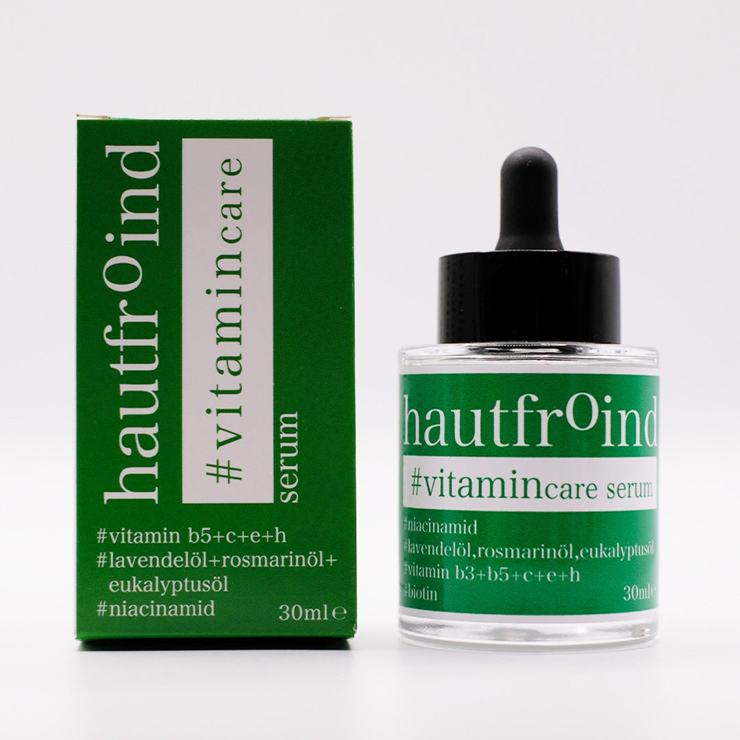 Hautfroind Vitamincare Serum – vitaminreiche Hautpflege und Gesichtspflege mit Niacinamid, Vitamin C & E. Hellt dunkle Flecken auf, fördert die Kollagenproduktion & schützt vor freien Radikalen. Feuchtigkeitsspendende Formel mit Aloe Vera & Hyaluronsäure für strahlende, gesunde Haut. Die Flasche Hautfroind Vitamincare Serum steht neben der Verpackung frontal vor eine, weissen Hintergrund.