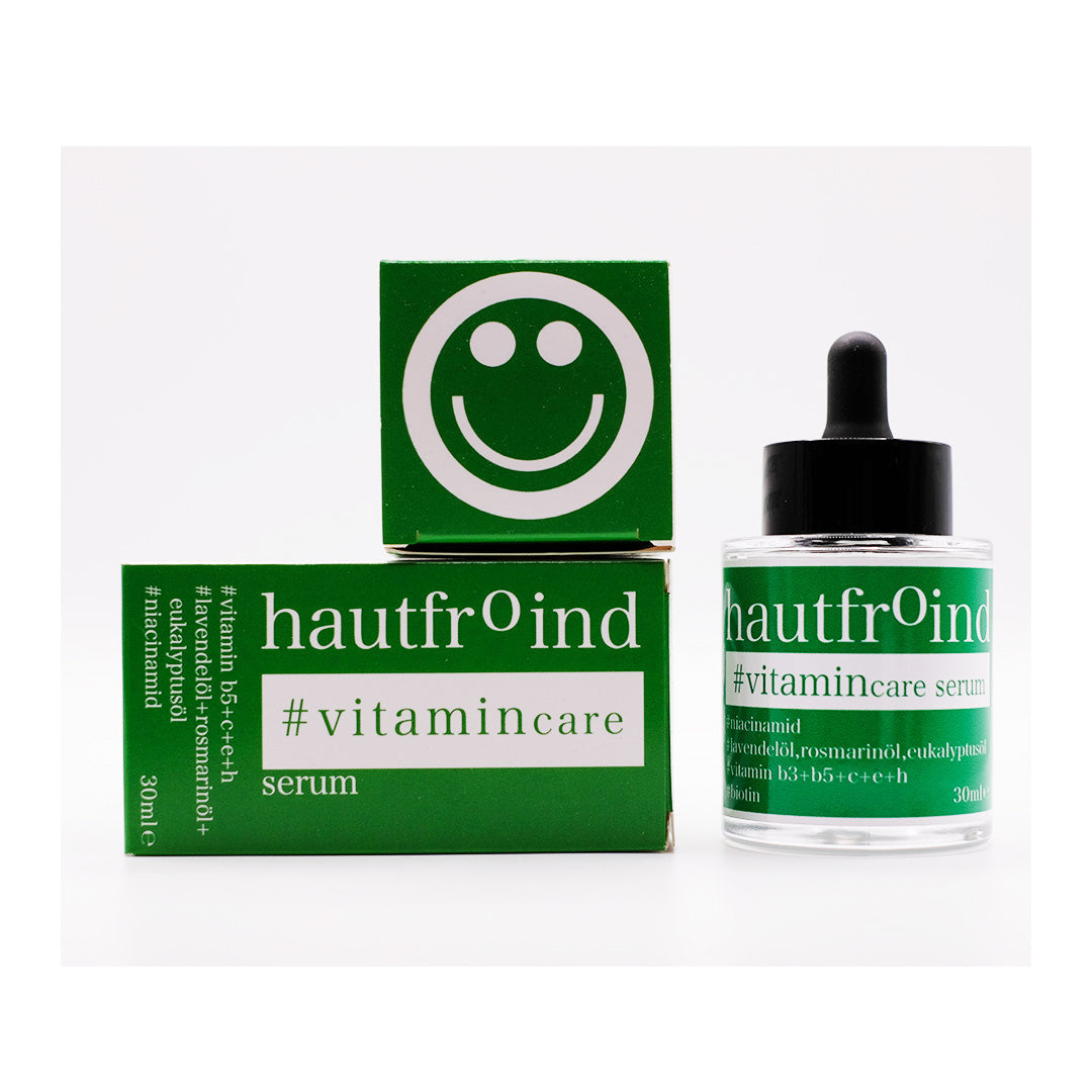 Hautfroind Vitamincare Serum – vitaminreiche Hautpflege und Gesichtspflege mit Niacinamid, Vitamin C & E. Hellt dunkle Flecken auf, fördert die Kollagenproduktion & schützt vor freien Radikalen. Feuchtigkeitsspendende Formel mit Aloe Vera & Hyaluronsäure für strahlende, gesunde Haut. Das Hautfroind Vitamincare Serum steht neben der liegenden Verpackung. Auf der liegenden Verpackung ist die Oberseite der Verpackung zu sehen, ein Smiley.
