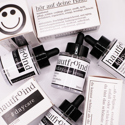 Hautfroind Daycare Serum – feuchtigkeitsspendende Hautpflege für das Gesicht mit Hyaluronsäure, Arganöl & Rosa Damascena Blütenwasser. Stärkt die Hautbarriere, verfeinert den Teint & sorgt für langanhaltende Feuchtigkeit. Leichte, schnell einziehende Gesichtspflege für strahlende Haut. Auf dem Foto sind die Flaschen des Daycare Serum zu sehen. Mit Verpackungen. Ein wenig wild angeordnet.