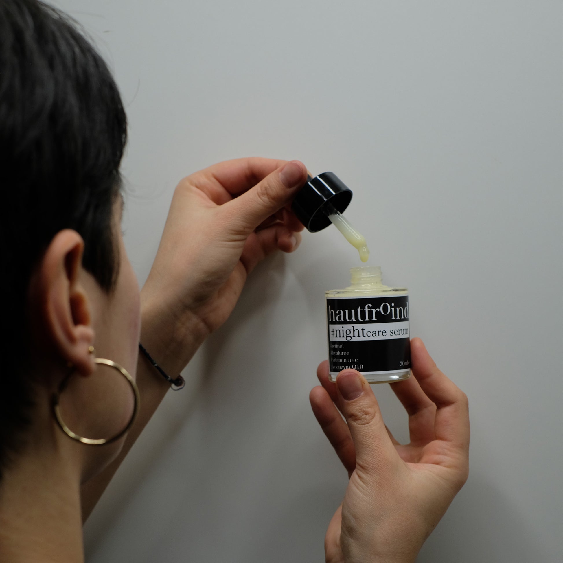 Hautfroind Nightcare Serum – regenerierende Hautpflege und Gesichtspflege mit Retinol, Coenzym Q10 & Hyaluronsäure. Fördert die Zellregeneration, stärkt die Kollagenproduktion & spendet Feuchtigkeit. Nährende Nachtpflege für glatte, erholte & strahlende Haut am Morgen. Es ist der Hinterkopf unseres Models zu sehen wie sie von der Pipette einen Tropfen in die Hautfroind nightcare Serum Flasche tropfen lässt. 